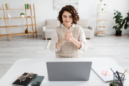 femme souriante montrant geste d'amitié tout en utilisant le langage des signes pendant la leçon en ligne sur ordinateur portable à la maison