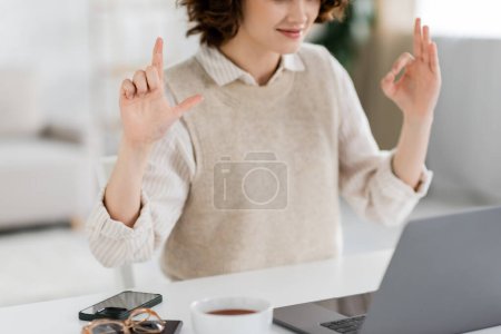 Foto de Vista recortada del profesor de lengua de signos que muestra signos del alfabeto durante la lección en línea en el ordenador portátil en casa - Imagen libre de derechos