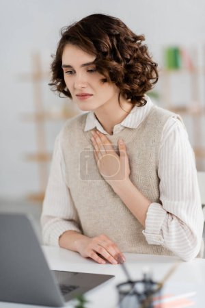 curly brunette woman showing please gesture on sign language while having online lesson on blurred laptop at home