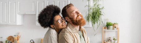 Cheerful african american woman in eyeglasses standing near boyfriend in kitchen, banner 