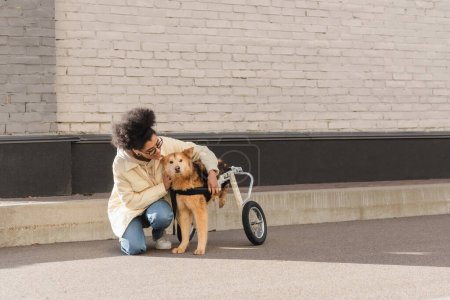 Smiling african american woman hugging dog with special needs on urban street 