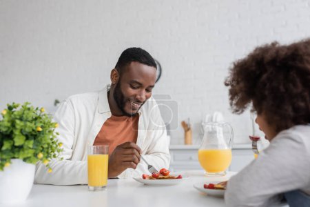 happy african american man having breakfast with curly daughter in kitchen 