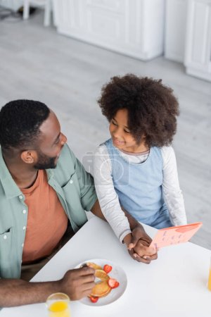 top view of curly african american girl holding greeting card near cheerful dad on fathers day 