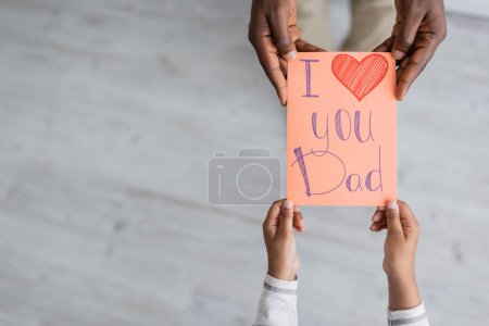 top view of cropped african american child holding greeting card with i love you dad lettering near man on fathers day 