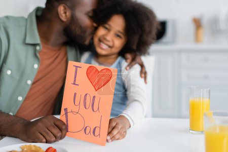 african american man kissing daughter and holding greeting card with i love you dad lettering on fathers day 