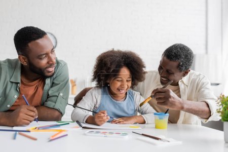 Alegres padres afroamericanos pintando con niños en casa 