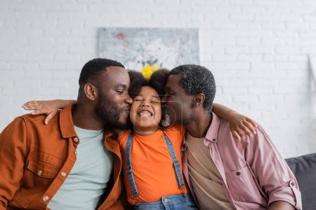 Téléchargez les photos : Père et grand-père afro-américain embrassant enfant gai dans le salon - en image libre de droit