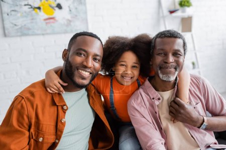 Carefree african american girl hugging father and grandpa in living room 