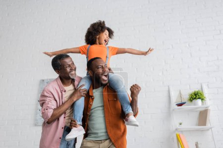 Téléchargez les photos : Homme afro-américain excité s'amuser avec sa fille et son père à la maison - en image libre de droit