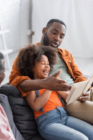 Afroamerikaner liest Buch bei fröhlicher Tochter und Vater zu Hause 