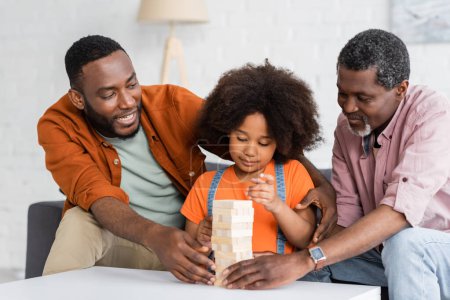 Cheerful african american father and grandpa playing wood blocks game with child at home 