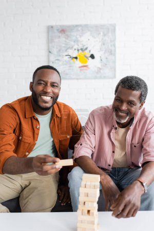 Cheerful african american father and son looking at camera near wood blocks game at home 