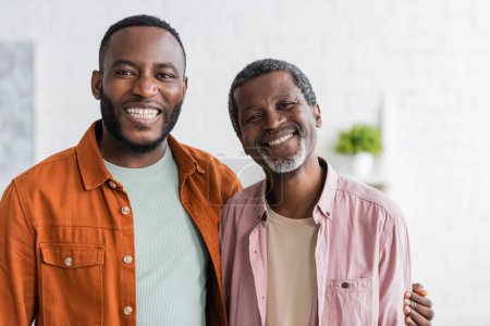 Positiver afrikanisch-amerikanischer Mann umarmt Vater und schaut zu Hause in die Kamera 