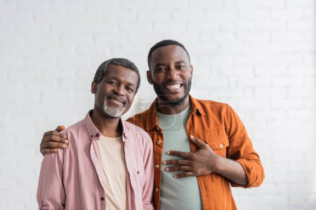 Carefree african american man hugging parent and looking at camera at home 