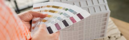 Téléchargez les photos : Vue recadrée du concepteur tenant palette de couleurs près du modèle de maison résidentielle dans le bureau, bannière - en image libre de droit