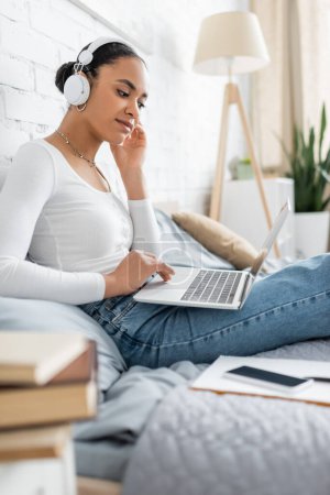 junge afrikanisch-amerikanische Studentin in drahtlosen Kopfhörern mit Laptop, während sie online Vorlesung schaut 