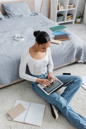 Hochwinkel-Ansicht von jungen afrikanisch-amerikanischen Studenten, die auf der Laptop-Tastatur tippen, während sie zu Hause online studieren 