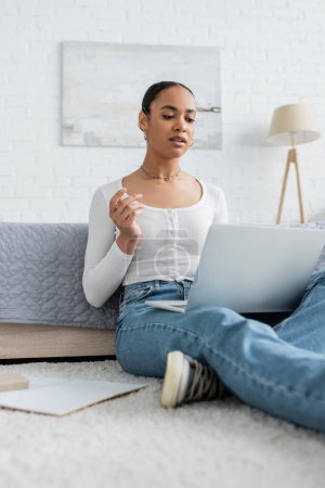 pretty african american woman in jeans watching webinar on laptop 