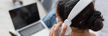 Foto de Vista superior del estudiante afroamericano que usa auriculares inalámbricos mientras escucha un libro de audio y usa una computadora portátil, pancarta - Imagen libre de derechos