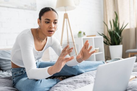 Estudiante afroamericano hablando durante webinar sobre computadora portátil borrosa en el dormitorio 