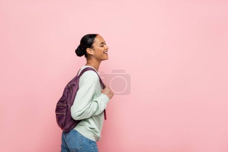 Foto de Estudiante afroamericano positivo con mochila de pie aislado en rosa - Imagen libre de derechos