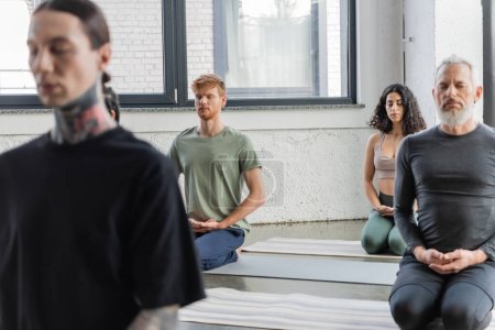 Interracial group of people meditating in Thunderbolt asana in yoga class 