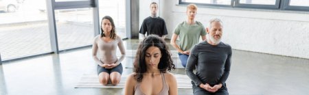 Gente multicultural meditando en Thunderbolt asana sobre esterillas de yoga en estudio, banner 
