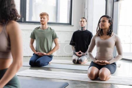 Mujer afroamericana sonriente meditando en Thunderbolt asana en grupo en clase de yoga 