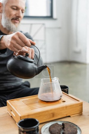 Blurred mature man pouring tea from pot in yoga class 