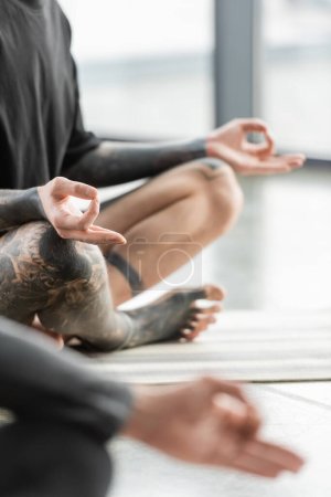 Téléchargez les photos : Vue recadrée de l'homme tatoué pratiquant mudra gyan en classe de yoga - en image libre de droit