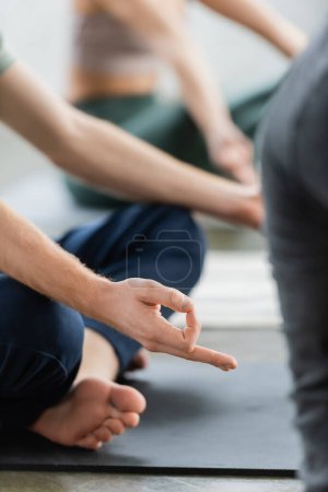 Téléchargez les photos : Vue recadrée de l'homme faisant mudra gyan sur tapis en cours de yoga - en image libre de droit