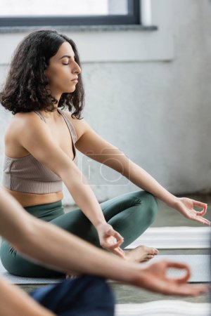 Middle eastern woman practicing gyan mudra on mat in yoga class 