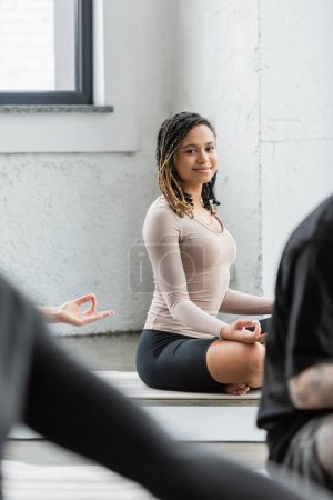 Unbekümmerte Afroamerikanerin schaut in die Kamera, während sie im Yoga-Kurs Gyan Mudra macht 