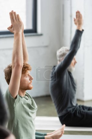 Young redhead man doing anjali mudra while sitting in yoga class 