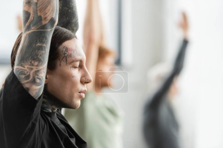 Téléchargez les photos : Vue latérale d'un jeune homme tatoué méditant en cours de yoga - en image libre de droit