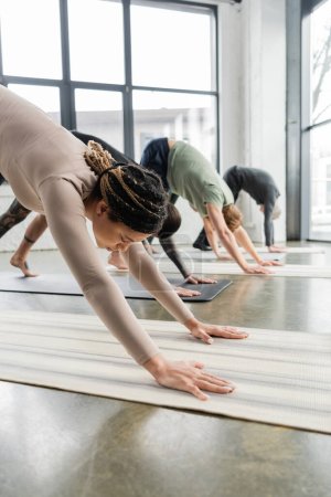 African american woman practicing Downward Facing Dog pose on mat in yoga class 