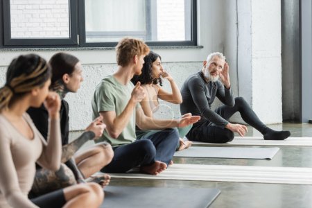Middle aged coach explaining nostril breathing to multiethnic group in yoga class 