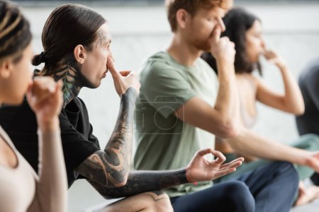 Tattooed man practicing nostril breathing and gyan mudra in yoga class 