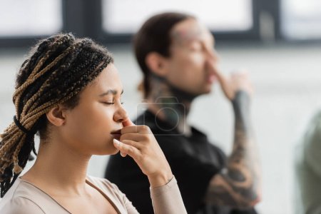 Joven mujer afroamericana practicando respiración nasal en clase de yoga 