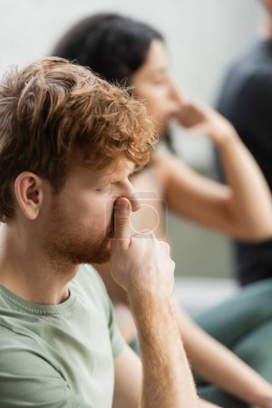 Redhead man practicing nostril breathing exercise in yoga studio  