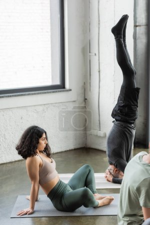Photo for Middle eastern woman in sportswear sitting on mat near people in yoga class - Royalty Free Image