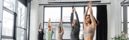 Las personas interraciales que practican Crescent Lunge posan en un estudio de yoga, pancarta 