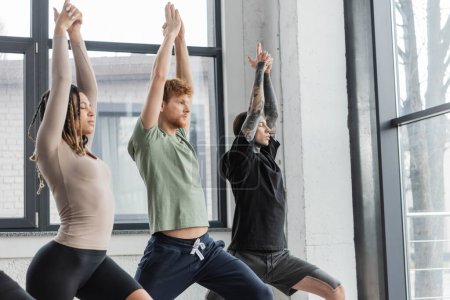 Jóvenes multiétnicos de pie en Crescent Lunge asana en clase de yoga 