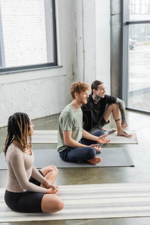 Téléchargez les photos : Jeunes gens souriants multiethniques parlant sur des nattes en cours de yoga - en image libre de droit