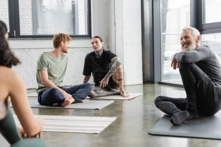 Téléchargez les photos : Les jeunes hommes parlent tout en étant assis sur des nattes en cours de yoga - en image libre de droit