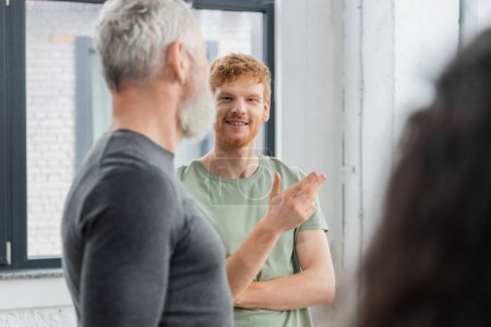 Smiling redhead man talking to blurred coach in yoga class 