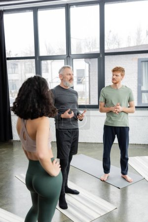 Middle aged coach talking to group of people in yoga studio 