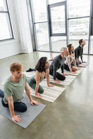 Grupo Interracial de personas practicando Media Paloma asana con los ojos cerrados en clase de yoga 