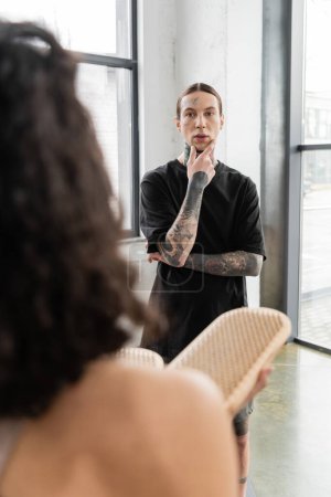 Tattooed man looking at blurred woman with sadhu board in yoga studio 