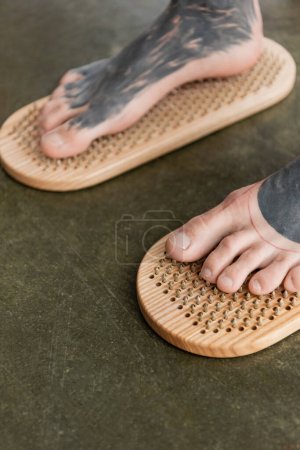 close up view of barefoot man with tattooed legs standing on sadhu nail board 